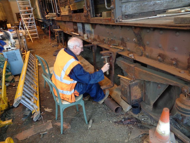 Geoff Horner, feet resting on the stove-pipe, chips away at the heavy corrosion on the running board brackets. It is not as comfortable as it appears Phil Hull has fashioned and painted the replacement boards. The originals had rotted away almost completely on this side.brPhotographer David BellbrDate taken 28022019