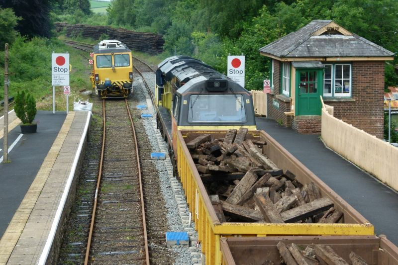 A busy scene at Okehampton the tamper stabled on the former down platform line  and a train of 20 'Falcon' bogie opens, with a Colas class 70 loco each end, being loaded with scrap sleepers for the NR Westbury materials recovery depot.  In the distance can be seen stacks of more scrap track that has been ferried by road rail vehicles with trailers, back to Okehampton from along the 11 miles of track that has been renewed with concrete sleepers and continuous welded rail, currently in the process of receiving its final ballasting and tamping.brPhotographer Dave EllisbrDate taken 07072021
