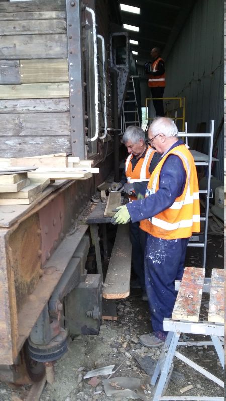 Patrick Doyle and John Davis marking out the cut for the last replacement plank on the side of the brake van. Ron Kirby in the background painting the Thumper's roof.brPhotographer David BellbrDate taken 23082018