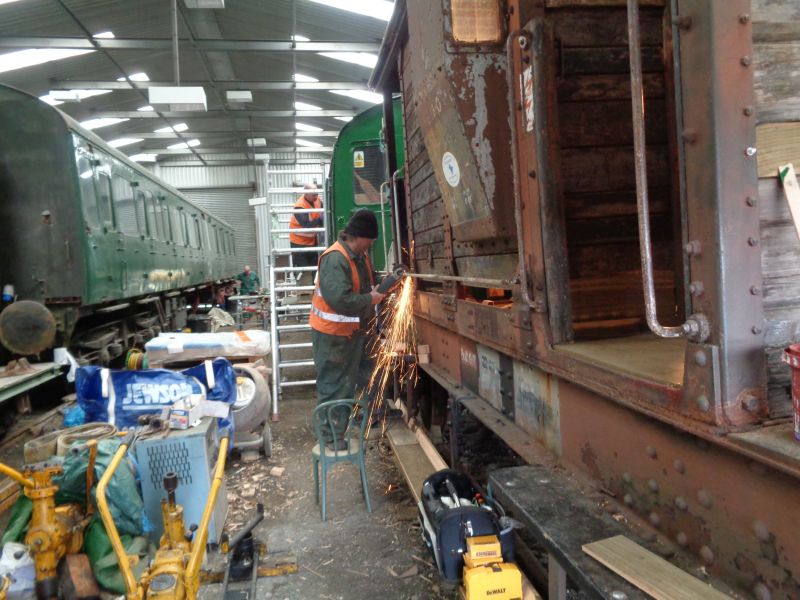 Grinding out yet another 70 year old rusted-in bolt on the brake van. Ron Kirby rubbing down the first topcoat on the Thumper whilst, in the far background, Nigel Green prepares a paint roller for the final topcoat. The chair in the picture was replaced, shortly after the photo was taken, with a pair of newly purchased steps.brPhotographer David BellbrDate taken 11102018