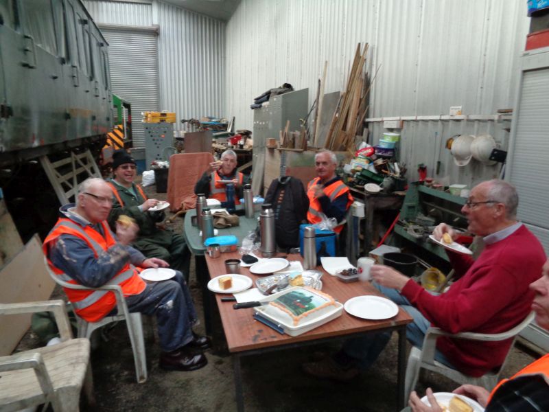 A depleted group of CW volunteers devour birthday cake before starting work. Apologies for the blurred shot, the photographer was laughing  For the eagle eyed, the decoration depicts an ex LSWR class T9 locomotive. These are fondly remembered as reliable, long lived and much admired workhorses in the Okehampton area until the early 1960's. Mr Drummond made exceedingly good cakes.brPhotographer David BellbrDate taken 18042019