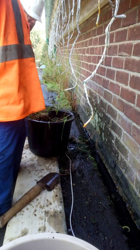 Close up of the drainage channel job partially done. The amount of vegetation can be seen in the uncleared section in the background. The white cable in the foreground was the connection to a CC TV camera which had been laid in the drainage channel. Dangling from the weatherboard are fairylights which we don't think are original.brPhotographer Jon KelseybrDate taken 04022019