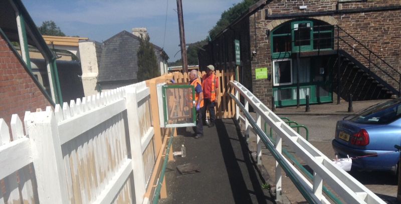 Stalwart volunteer Alan painting the fencing and notice case at the Okehampton station downside entrance, with Tom observing.brPhotographer Tony HillbrDate taken 08082020